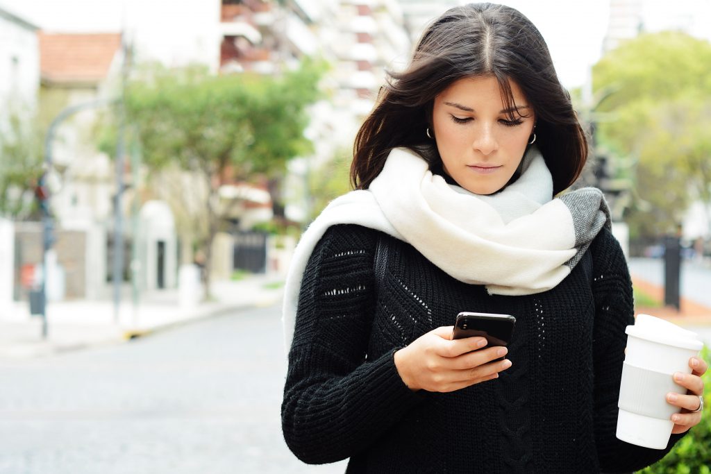 Women walking through the city and sending message with smartphone.