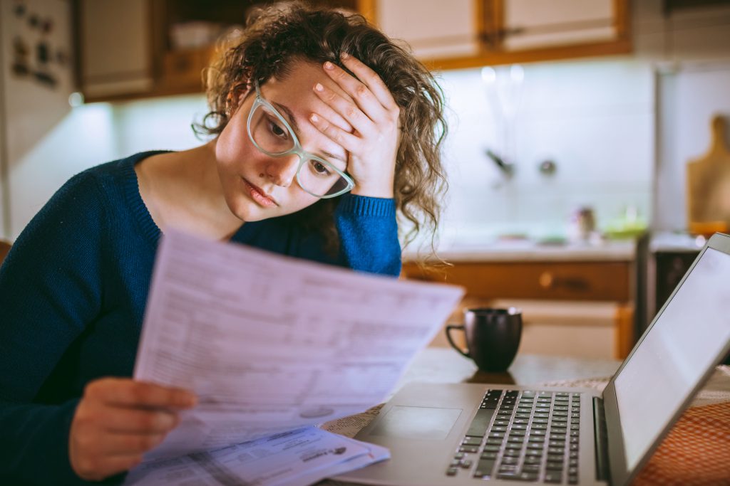 Woman going through bills at laptop at home, with serious expression